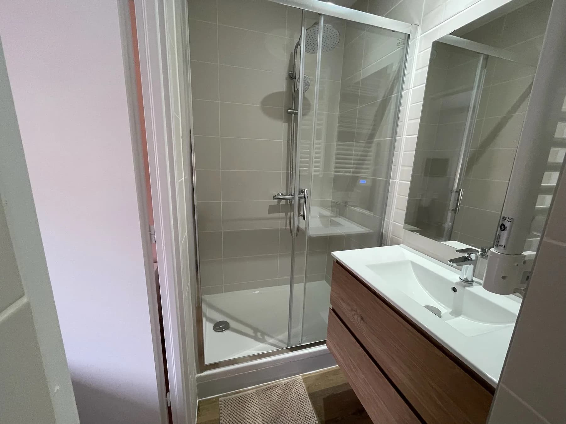 Salle d’eau claire avec douche vitrée, vasque blanche et meuble en bois.