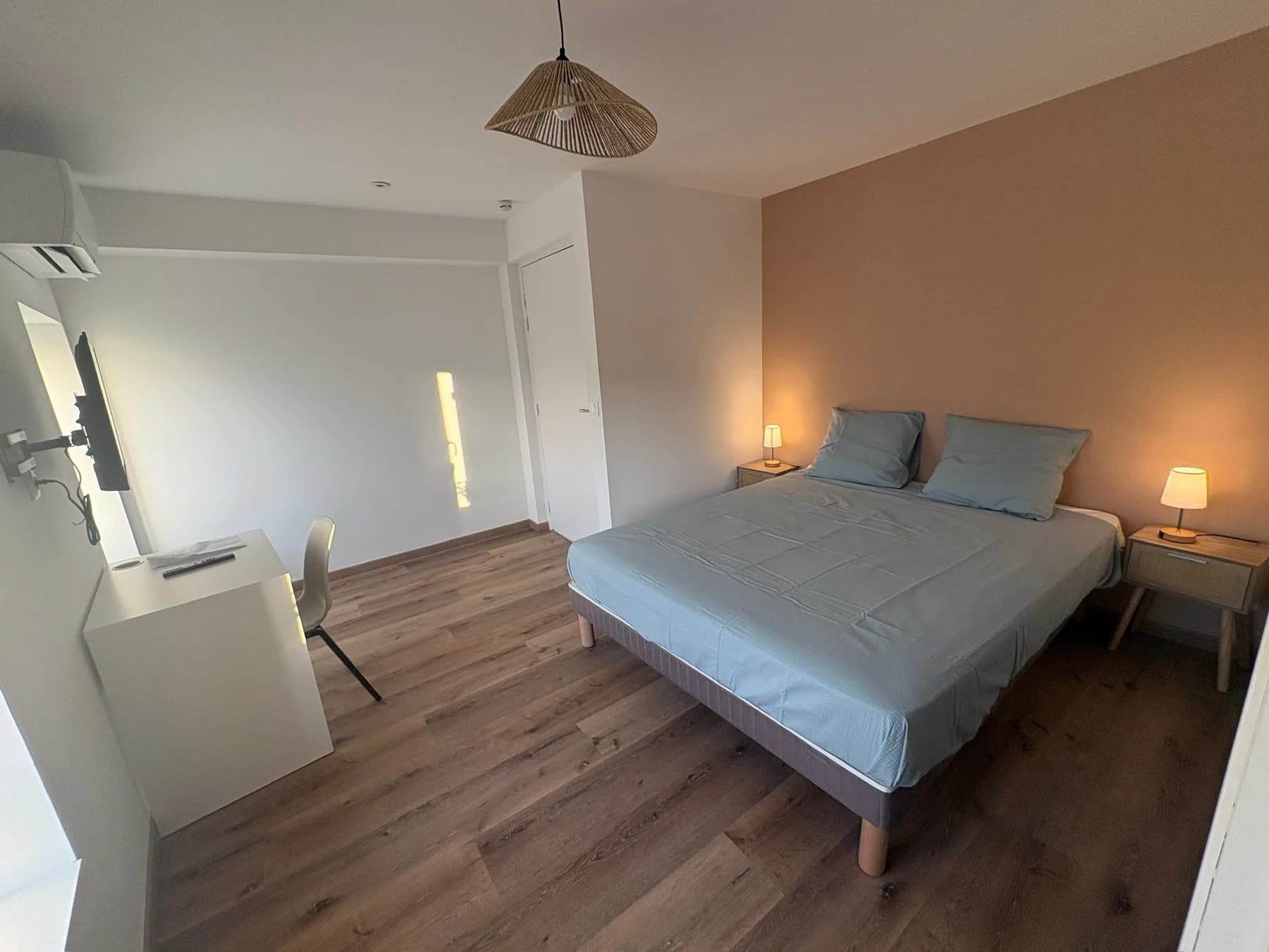 Chambre double avec linge de lit gris, bureau, télévision et climatisation.