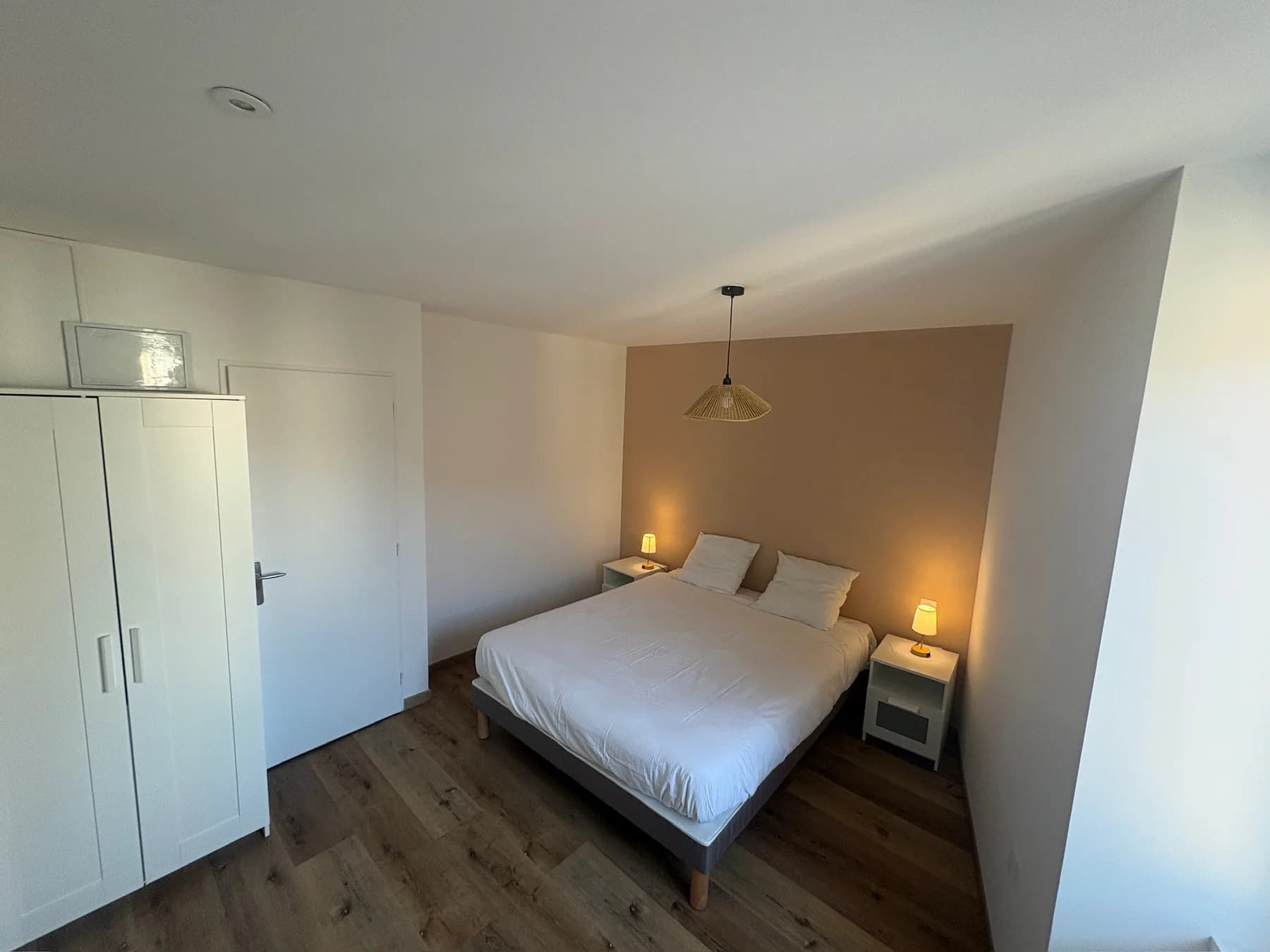 Chambre double aux tons clairs, avec mur beige, rangements et lampes de chevet.