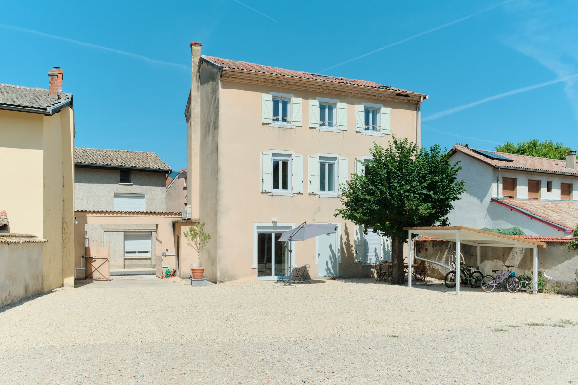 Cour gravillonnée de Villa 61 avec stationnement, terrasse ombragée et abri vélos.