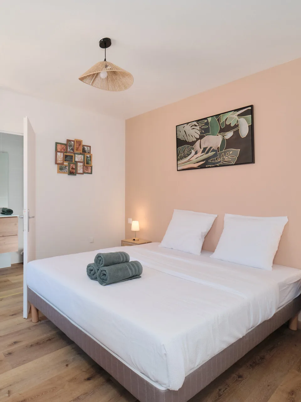Chambre double aux tons rose poudré avec lit préparé et salle d’eau en arrière-plan.